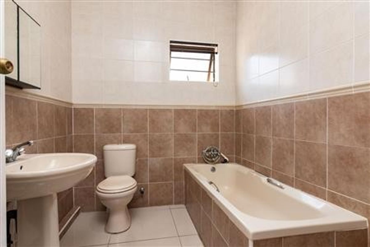 A functional bathroom featuring a pedestal basin, a standard toilet, and a tiled bathtub with wall-mounted fixtures.