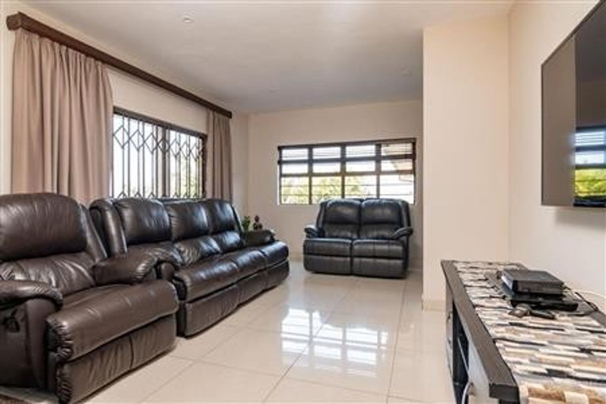 A spacious living room featuring large windows with security bars, tiled flooring, and recessed lighting, providing a bright and functional living space.