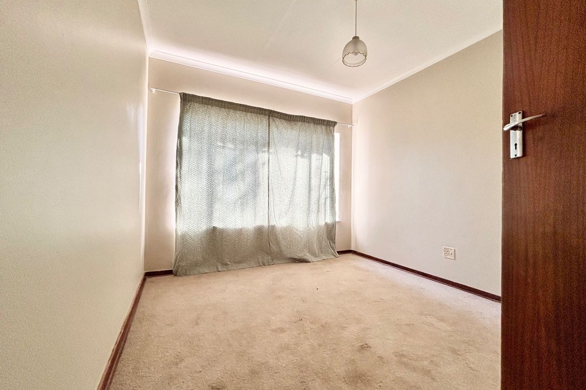 An empty bedroom featuring neutral walls, carpeted flooring, and a window with curtains, offering a blank canvas for personalization.