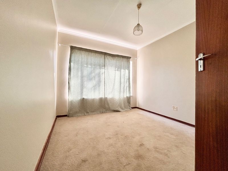 An empty bedroom featuring neutral walls, carpeted flooring, and a window with curtains, offering a blank canvas for personalization.