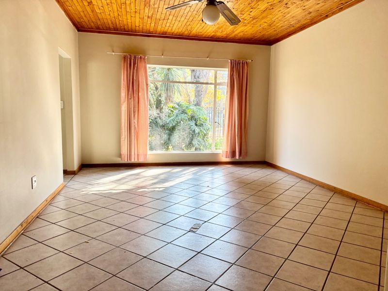 An empty living room featuring ceramic floor tiles, a timber tongue and groove ceiling, and a ceiling fan with natural light.