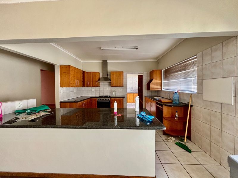 Functional kitchen featuring granite countertops, wooden cabinetry, a stainless steel extractor fan, and tiled flooring with an adjacent scullery area.