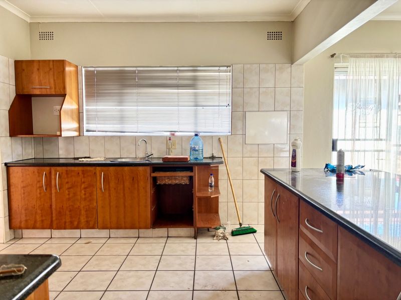 A functional kitchen featuring wood-finish cabinetry, granite countertops, and tiled flooring, offering a practical layout with ample storage and workspace.