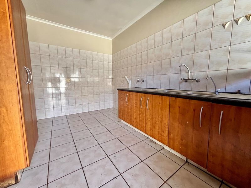 A functional scullery or laundry area featuring tiled walls and flooring, built-in wooden cabinetry, and a stainless steel sink with plumbing connections.