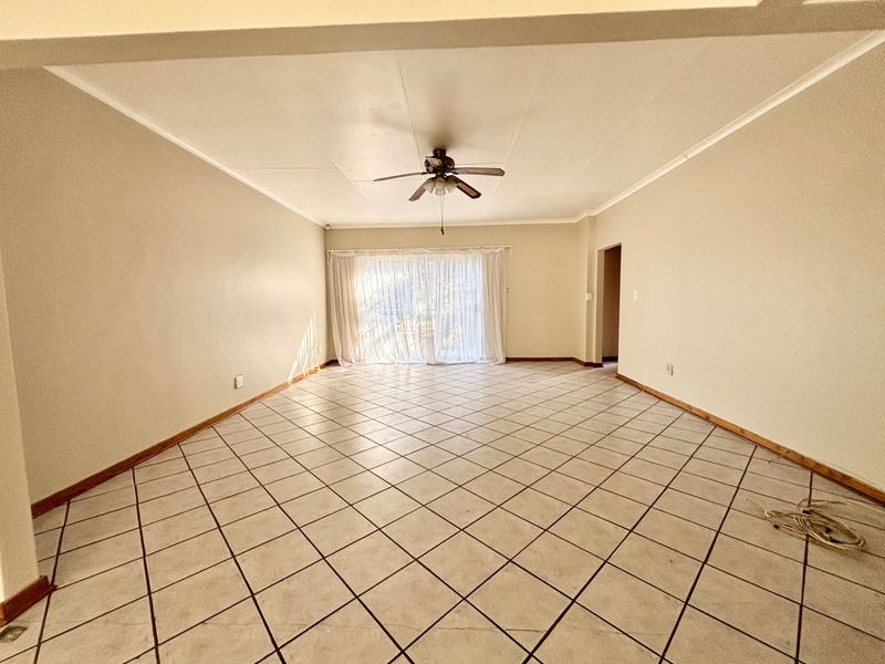 A spacious, empty living room featuring neutral tiled flooring, a ceiling fan, and a large sliding glass door providing natural light.