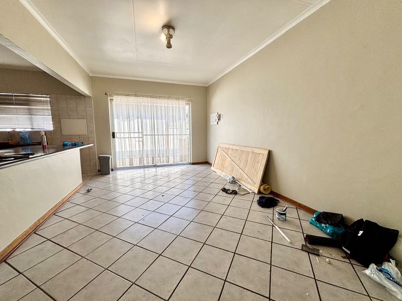 An open-plan living area featuring tiled flooring, a breakfast bar, and a sliding glass door leading to the exterior.