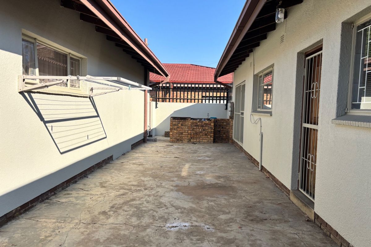 Rear exterior courtyard area featuring a brick braai, concrete paving, and wall-mounted clothesline between two building sections.