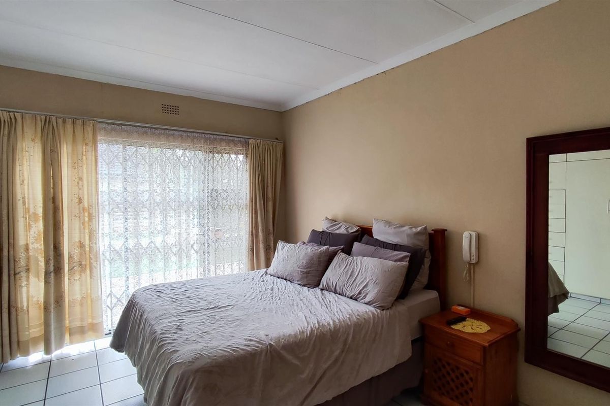 A bedroom featuring tiled flooring, a large window with security gate, and a wall-mounted intercom system.