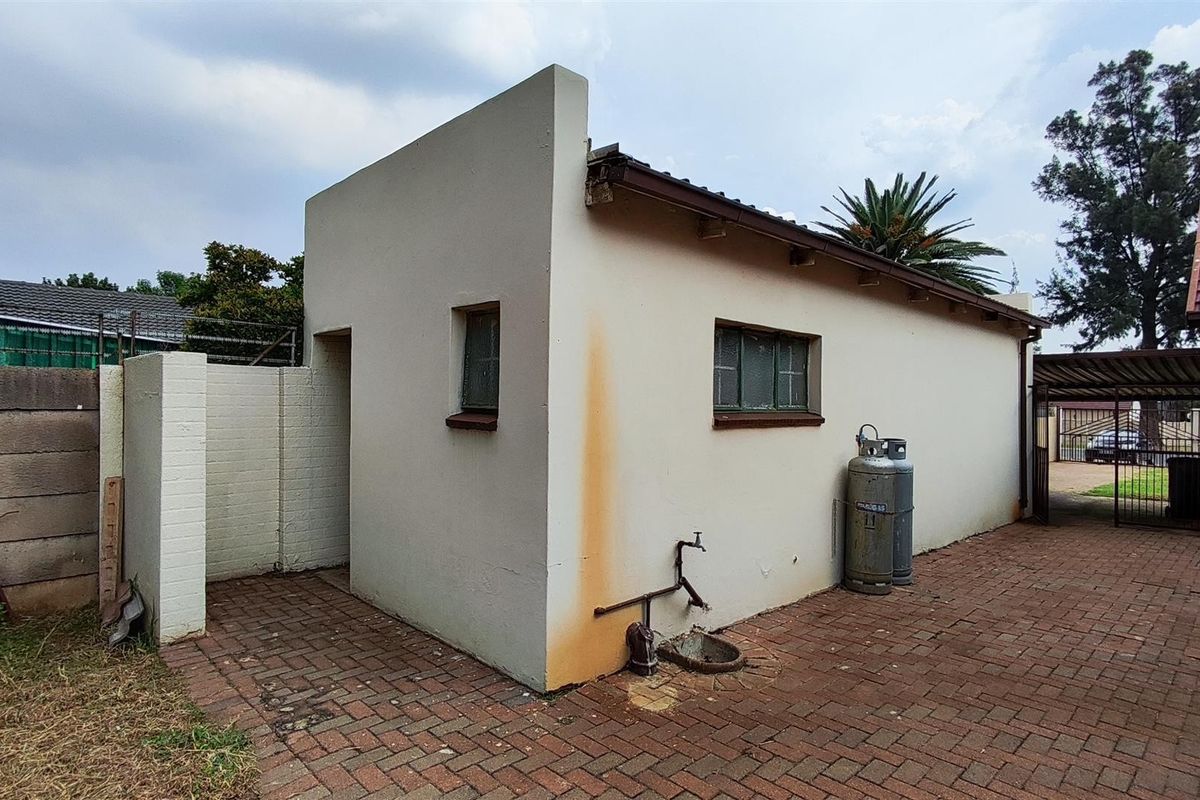 Exterior view of a utility structure featuring brick paving, a wall-mounted outdoor tap, and gas cylinder storage.