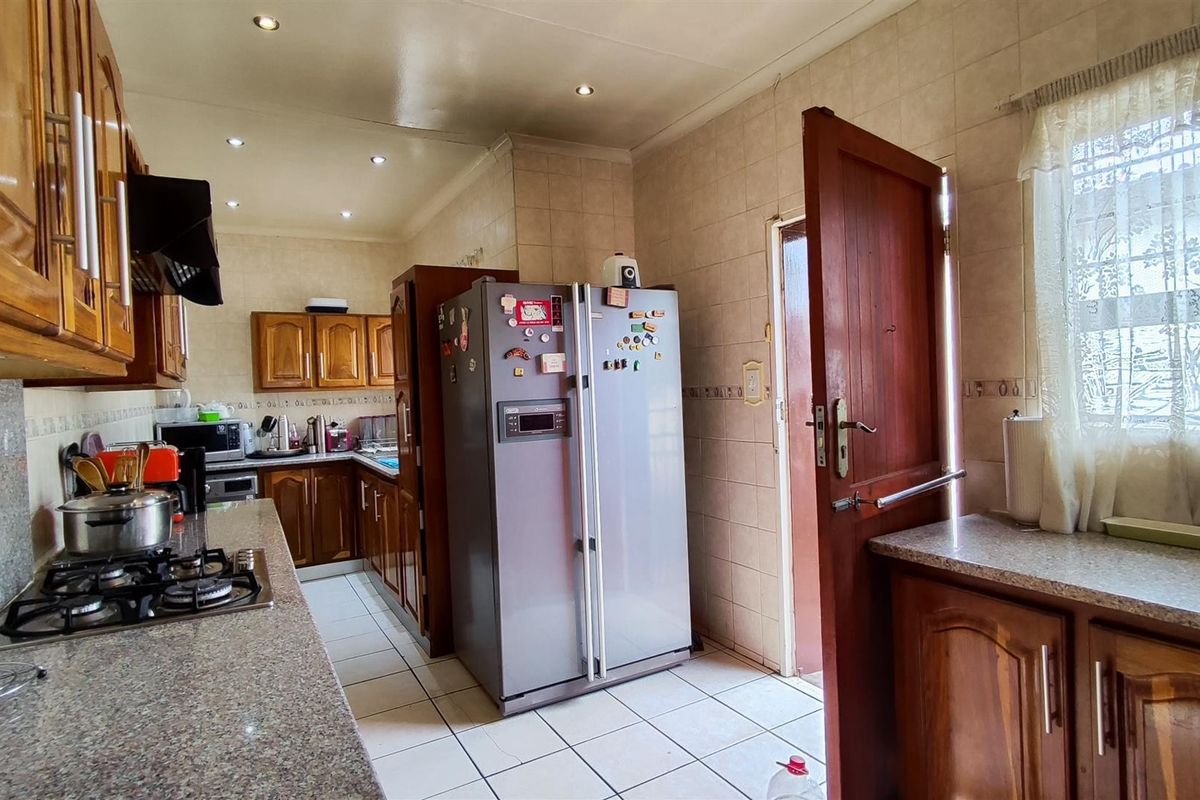 A functional kitchen featuring wooden cabinetry, granite countertops, a gas hob, and tiled flooring with direct access to an exterior door.