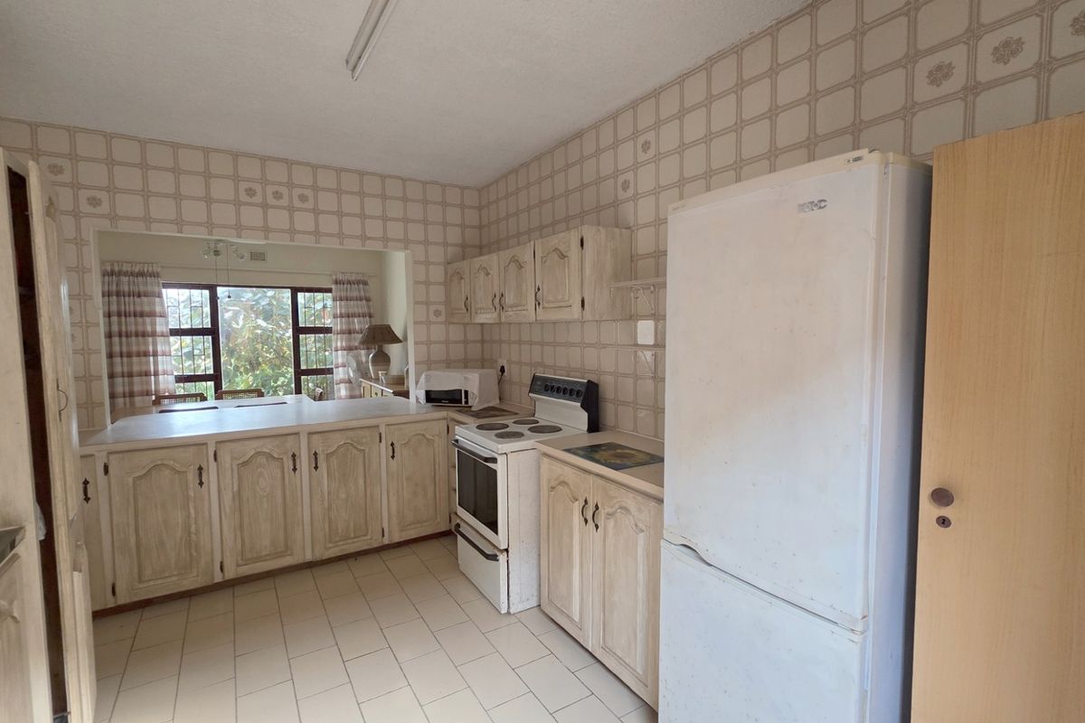 A dated kitchen featuring traditional cabinetry, tiled walls, and a breakfast bar opening into the adjacent living area.