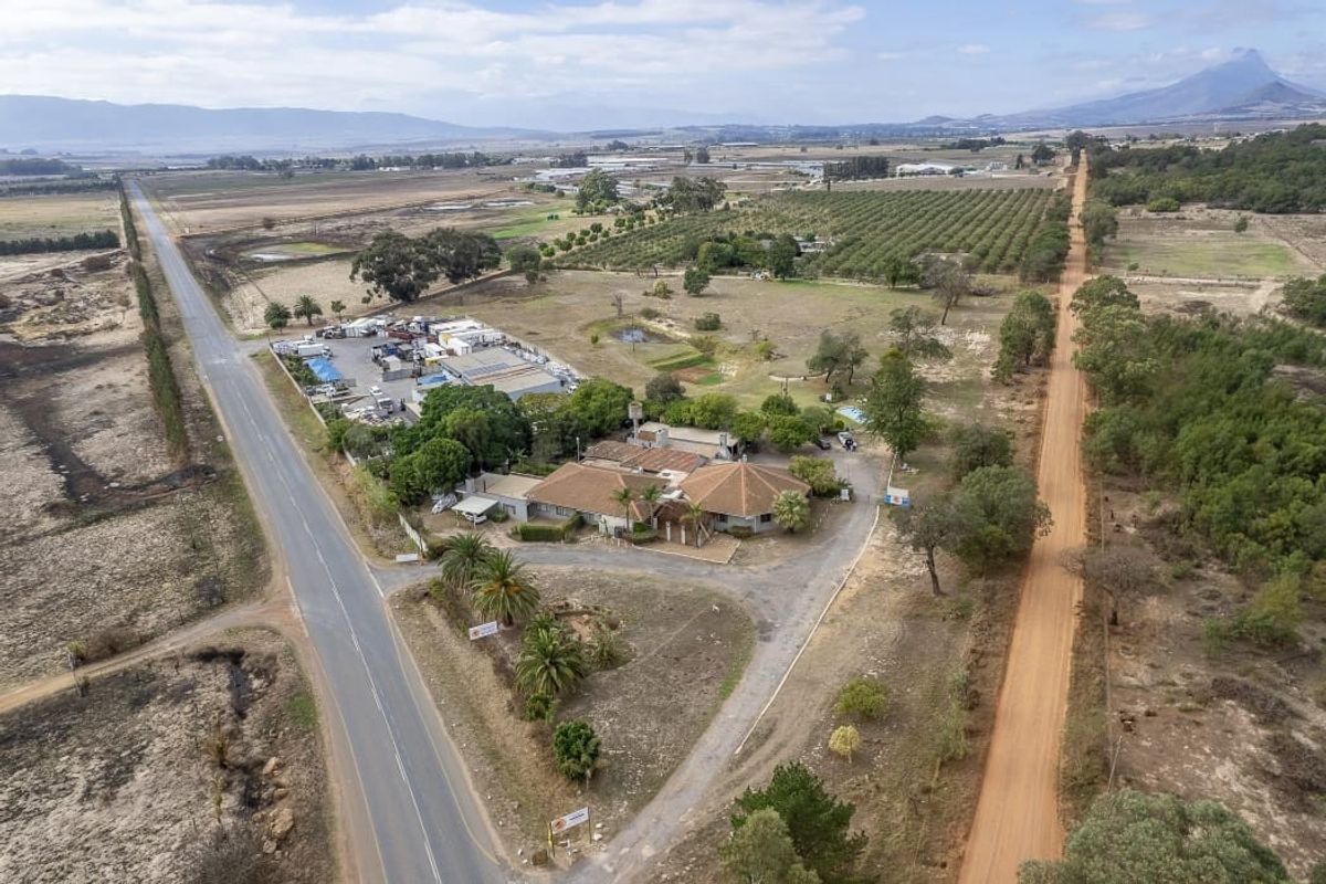 Aerial view of a farm property featuring a main residence, outbuildings, swimming pool, and extensive surrounding agricultural land with road access.
