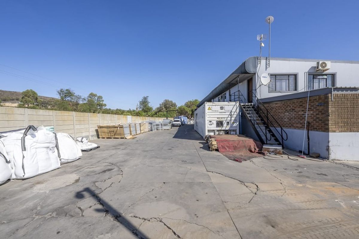 Rear exterior view of the farm property featuring a large concrete yard, boundary wall, and external staircase access to the building.