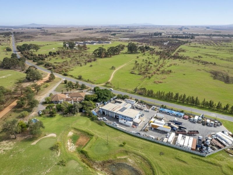 Aerial view of a farm property featuring a main residence, an industrial warehouse facility, and extensive surrounding agricultural land.