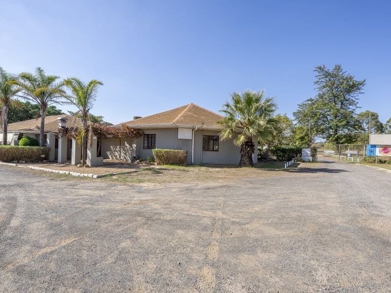 Front exterior view of a farm property featuring a single-story building with a tiled roof, covered patio area, and a large gravel driveway.