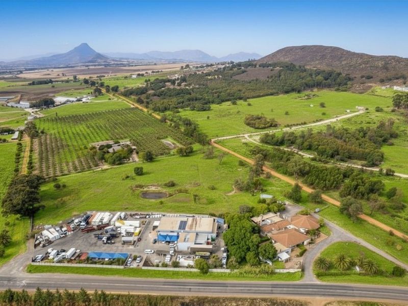 Aerial view of a large farm property featuring a main residence, extensive outbuildings, orchards, and surrounding agricultural land with mountain views.