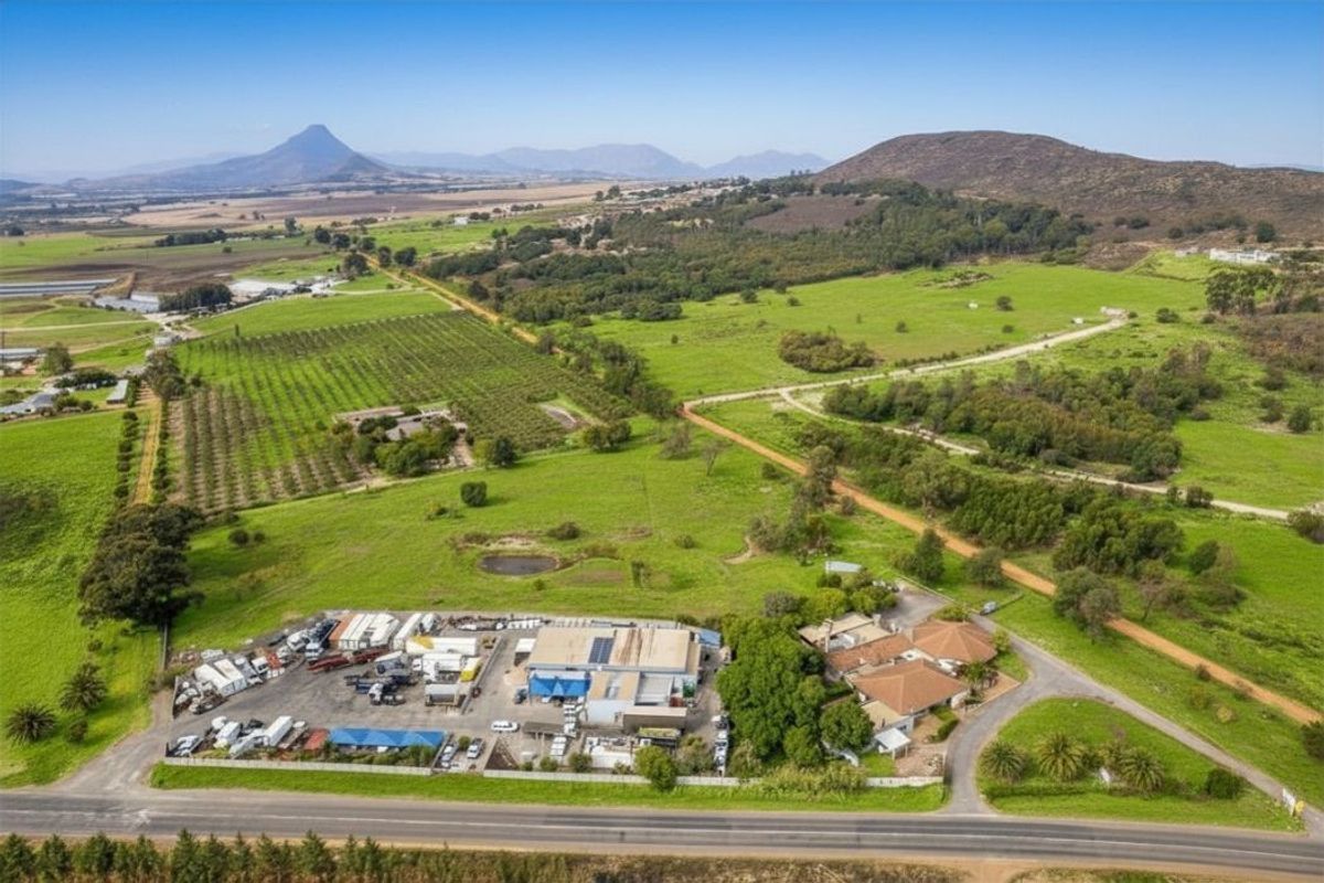 Aerial view of a large farm property featuring a main residence, extensive outbuildings, orchards, and surrounding agricultural land with mountain views.