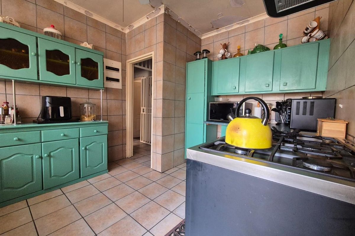 A dated kitchen featuring green cabinetry, tiled walls and flooring, and a gas stove. The ceiling requires repair and cosmetic attention.