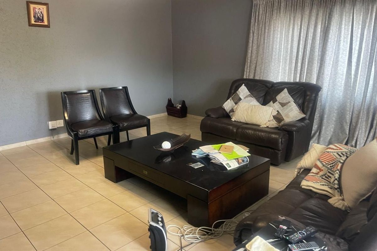 A spacious living room featuring neutral tiled flooring, grey painted walls, and decorative ceiling cornicing, providing a comfortable and functional living space.