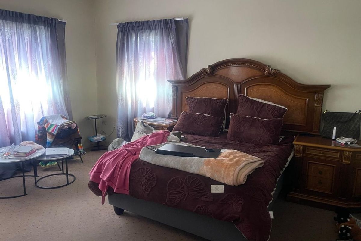 A spacious bedroom featuring neutral walls, carpeted flooring, and dual windows with curtain treatments.