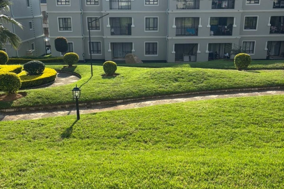 A view of the apartment complex exterior featuring well-maintained lawns, landscaped garden beds, paved pathways, and private balconies.