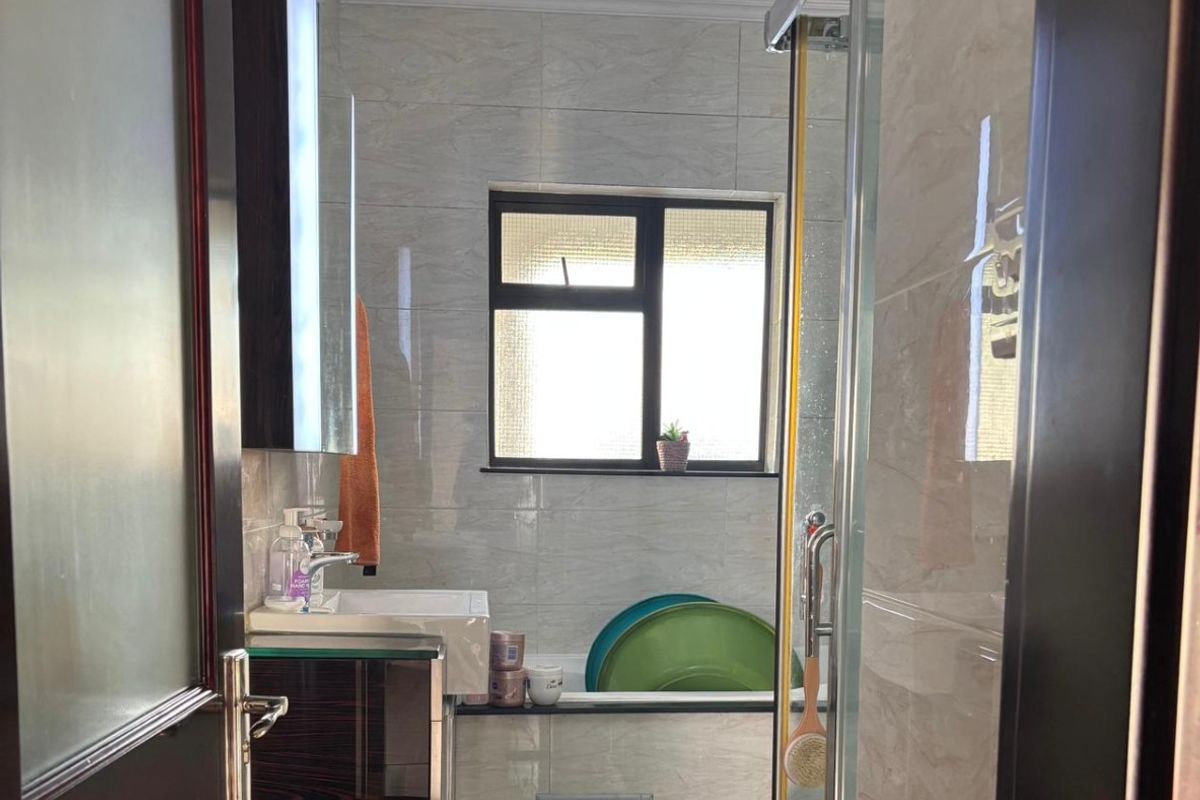 A compact bathroom featuring tiled walls, a vanity cabinet with basin, and a glass-enclosed shower area.