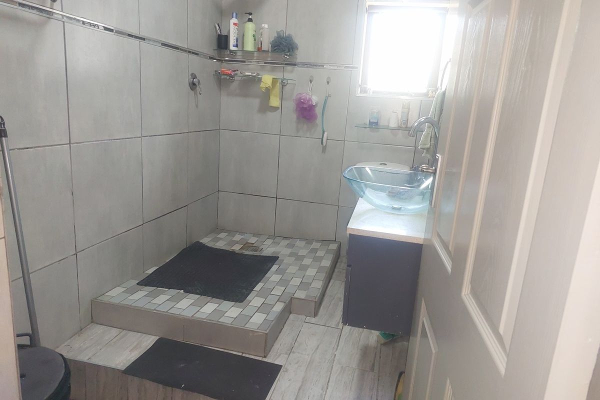 A functional bathroom featuring a raised shower area with tiled finishes, a glass vessel sink, and a vanity unit.