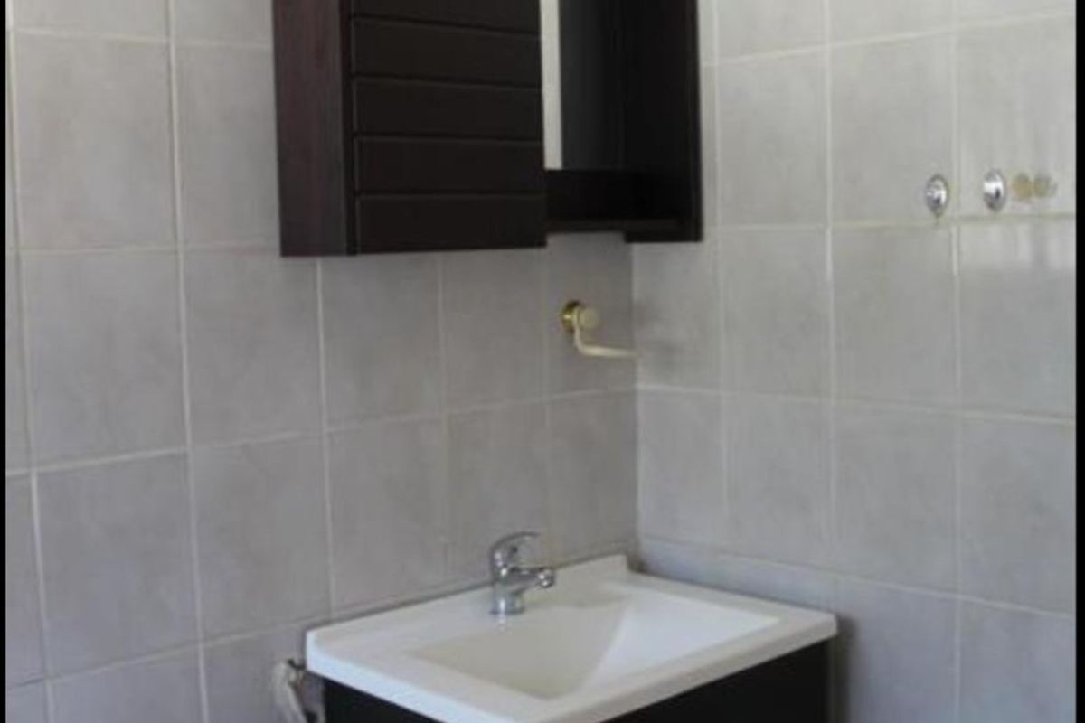 A functional bathroom featuring a dark wood vanity with a white basin, wall-mounted storage cabinet, and full-height wall tiling.