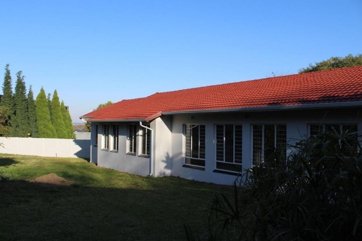 Rear view of the house featuring a red tiled roof, white exterior walls, and security bars on the windows, set against a grassy backyard.