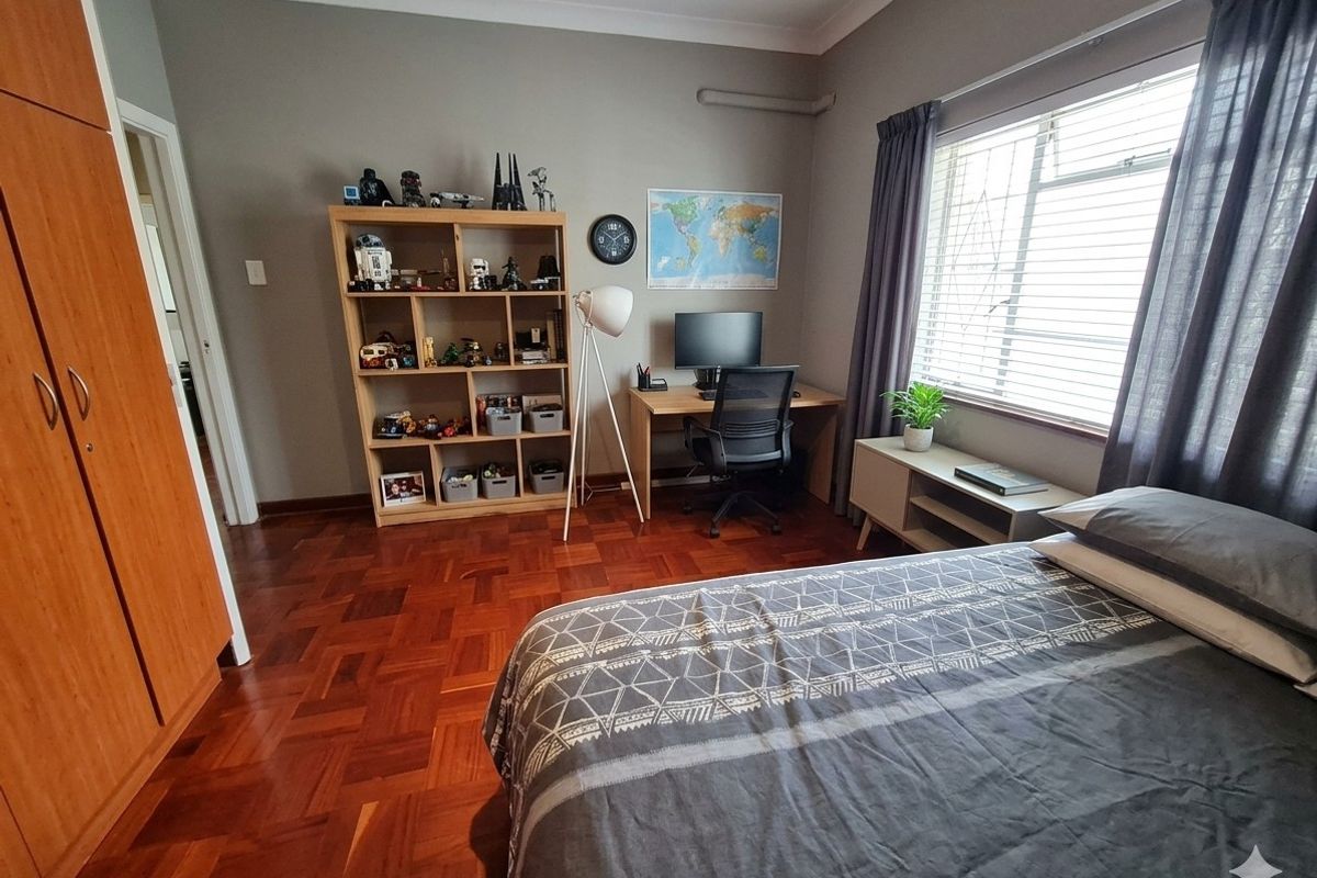 A well-maintained bedroom featuring classic parquet flooring, a built-in wardrobe, and large windows with security bars, offering a functional and comfortable living space.