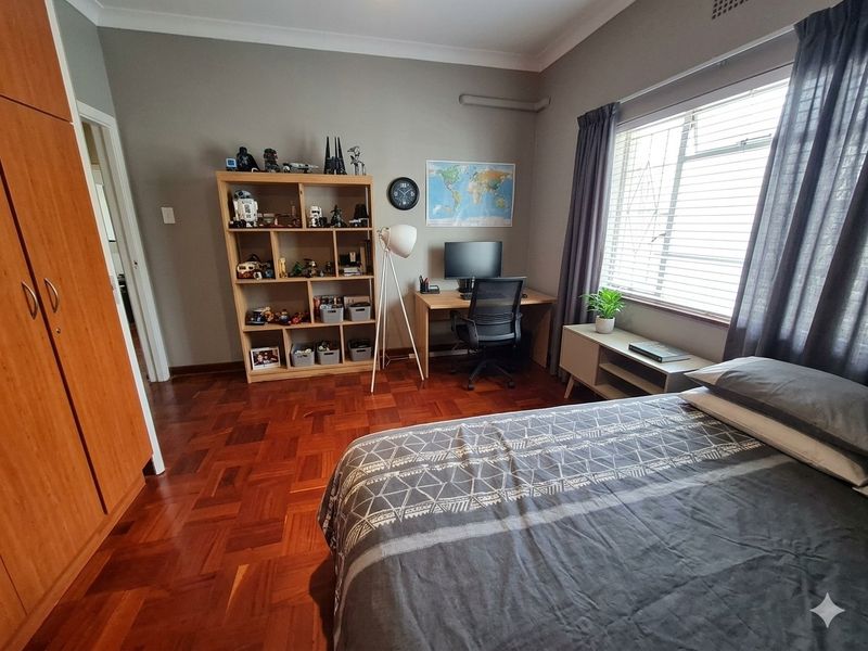 A well-maintained bedroom featuring classic parquet flooring, a built-in wardrobe, and large windows with security bars, offering a functional and comfortable living space.