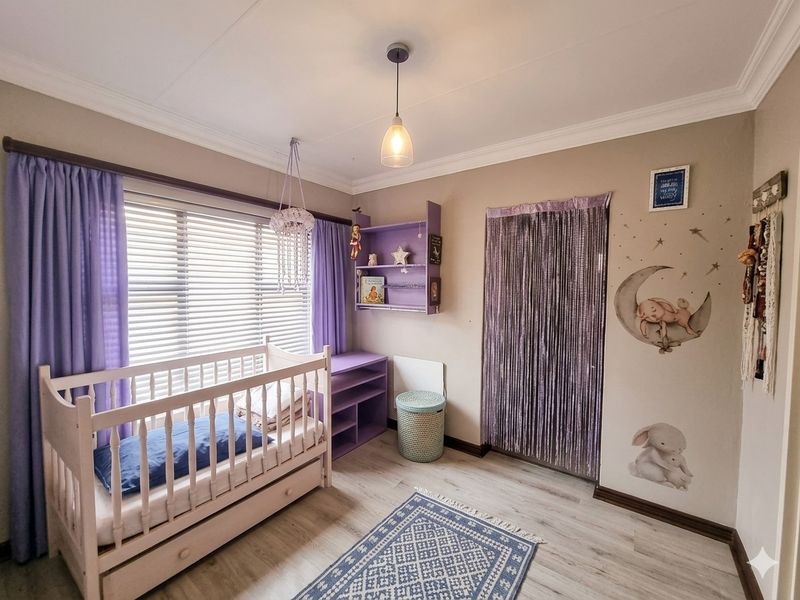A well-maintained bedroom featuring laminate flooring, cove cornicing, built-in shelving, and venetian blinds, currently styled as a nursery.