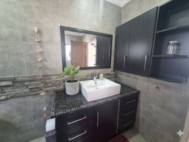 Modern bathroom vanity featuring a vessel sink, dark cabinetry, and contemporary grey wall tiling.