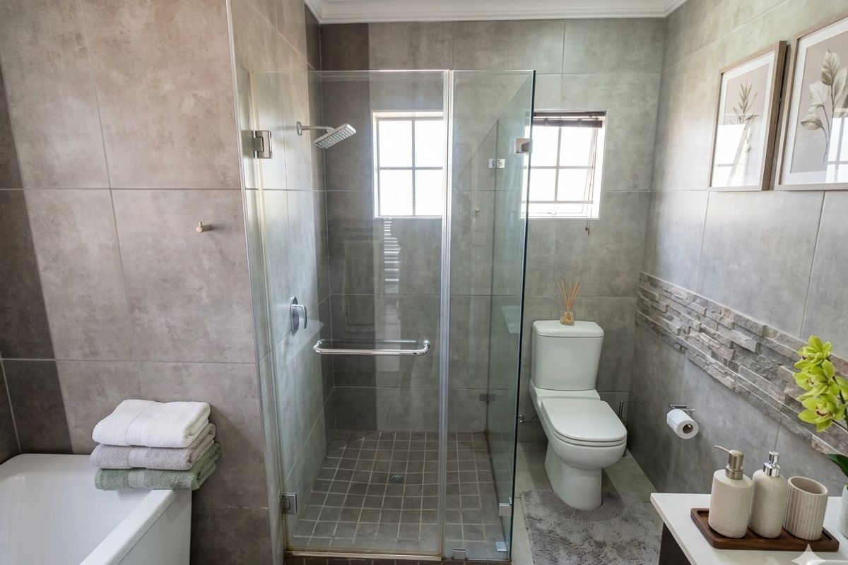Modern bathroom featuring a glass-enclosed shower, bathtub, and neutral grey tiling with a decorative stone accent wall.