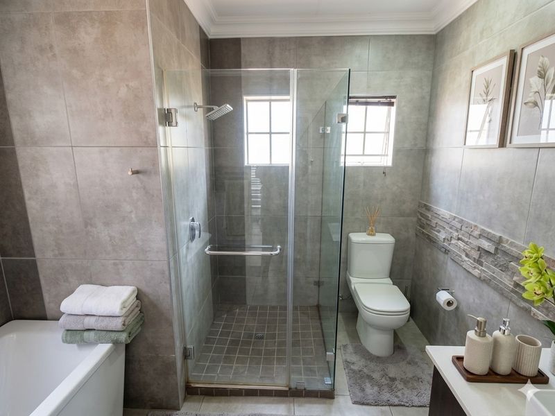 Modern bathroom featuring a glass-enclosed shower, bathtub, and neutral grey tiling with a decorative stone accent wall.