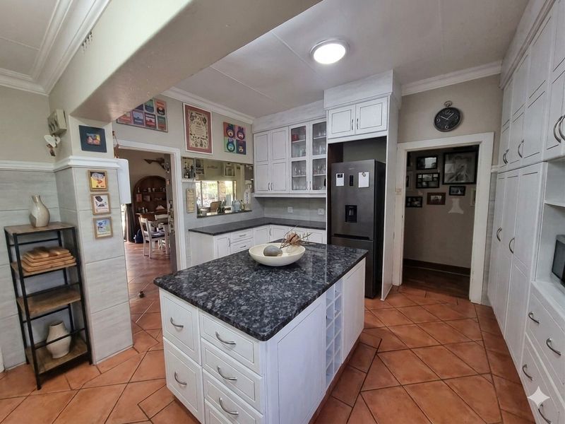 A well-maintained kitchen featuring a central island with granite countertops, ample built-in cabinetry, and terracotta-style floor tiles, connecting to adjacent living spaces.