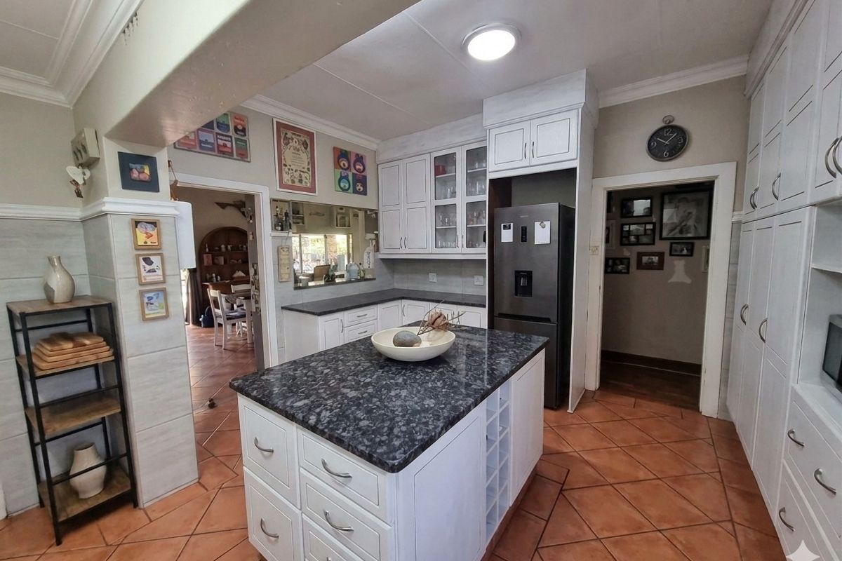 A well-maintained kitchen featuring a central island with granite countertops, ample built-in cabinetry, and terracotta-style floor tiles, connecting to adjacent living spaces.