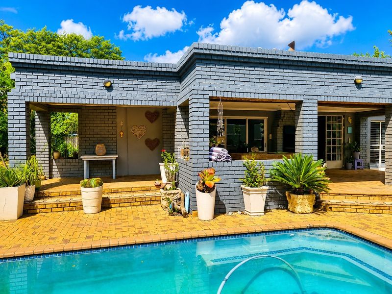 A well-maintained outdoor pool area featuring a paved patio, covered veranda, and painted brick exterior walls, ideal for outdoor relaxation and entertainment.