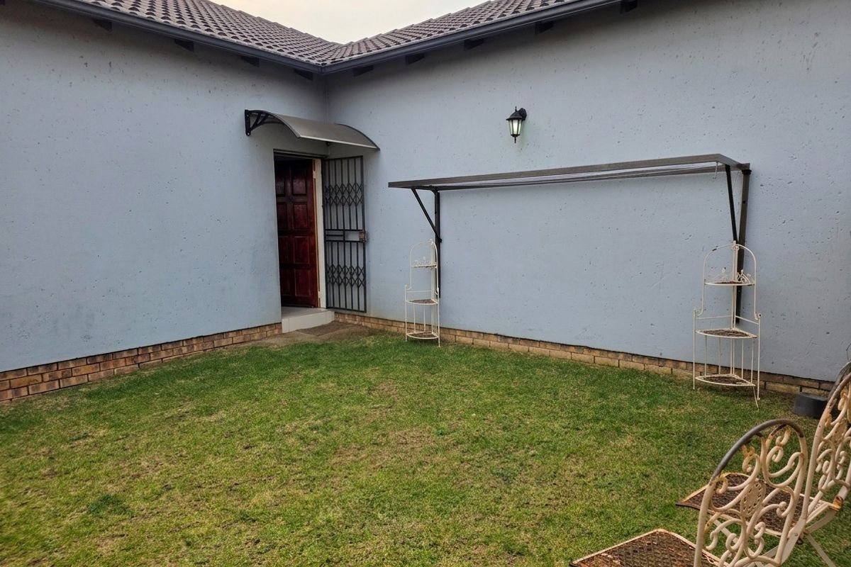 A private rear courtyard area featuring a small lawn, security gate access, and a wall-mounted clothesline.