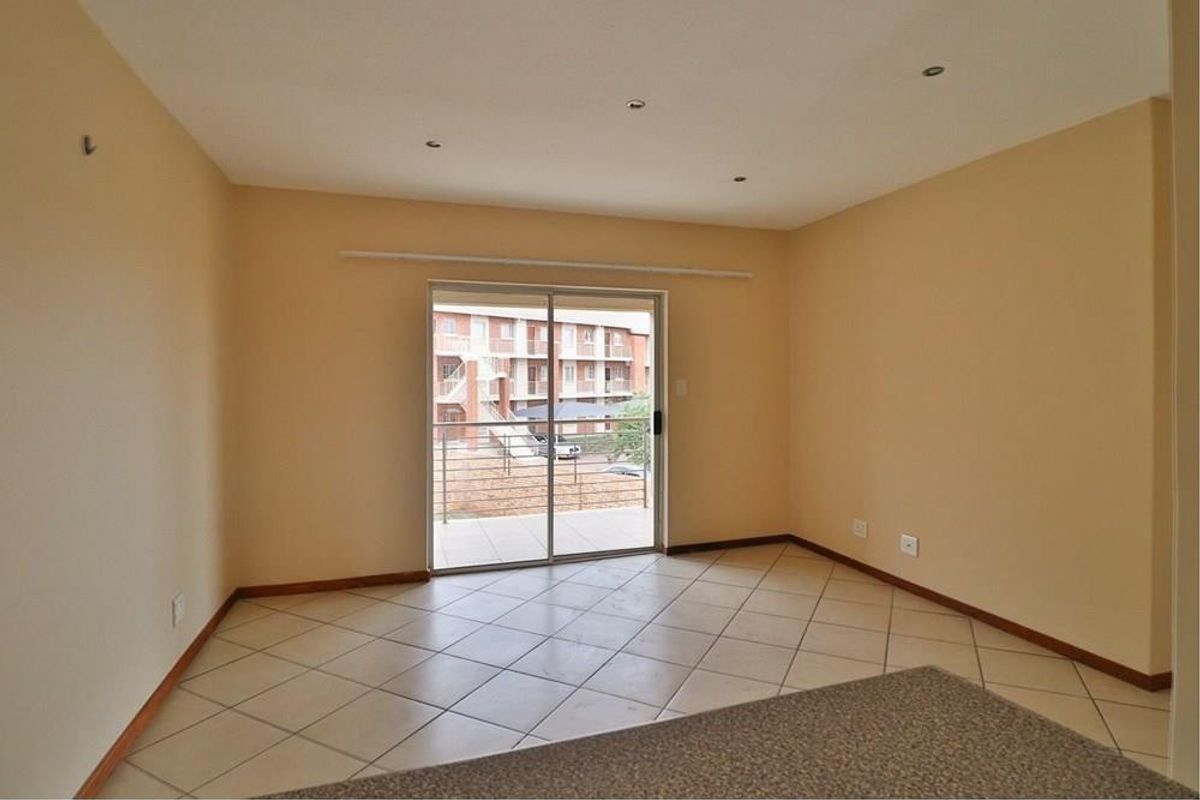 An empty, neutrally painted living room featuring tiled flooring and a sliding glass door that opens onto a balcony.