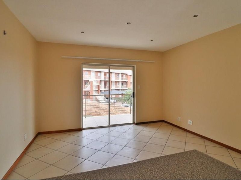 An empty, neutrally painted living room featuring tiled flooring and a sliding glass door that opens onto a balcony.