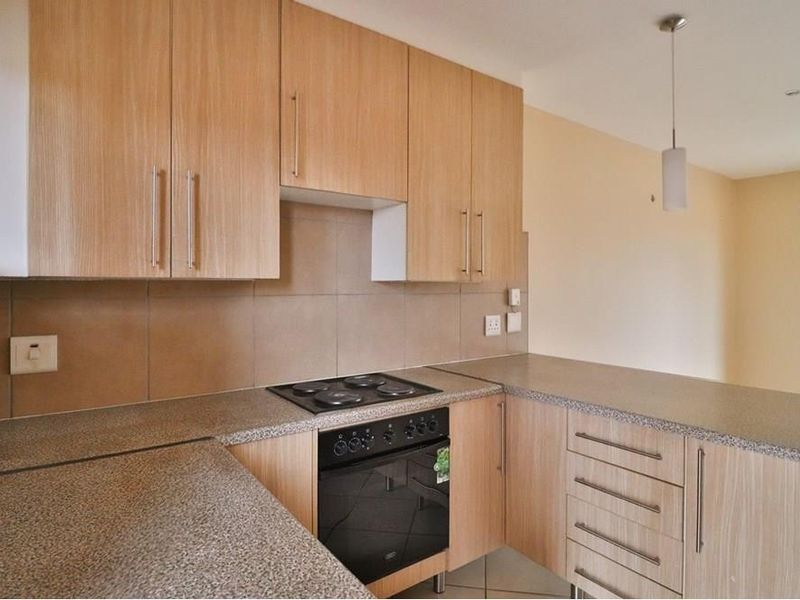 A functional kitchen featuring light wood-finish cabinetry, stone-look countertops, a built-in electric oven and hob, and a neutral tiled backsplash.
