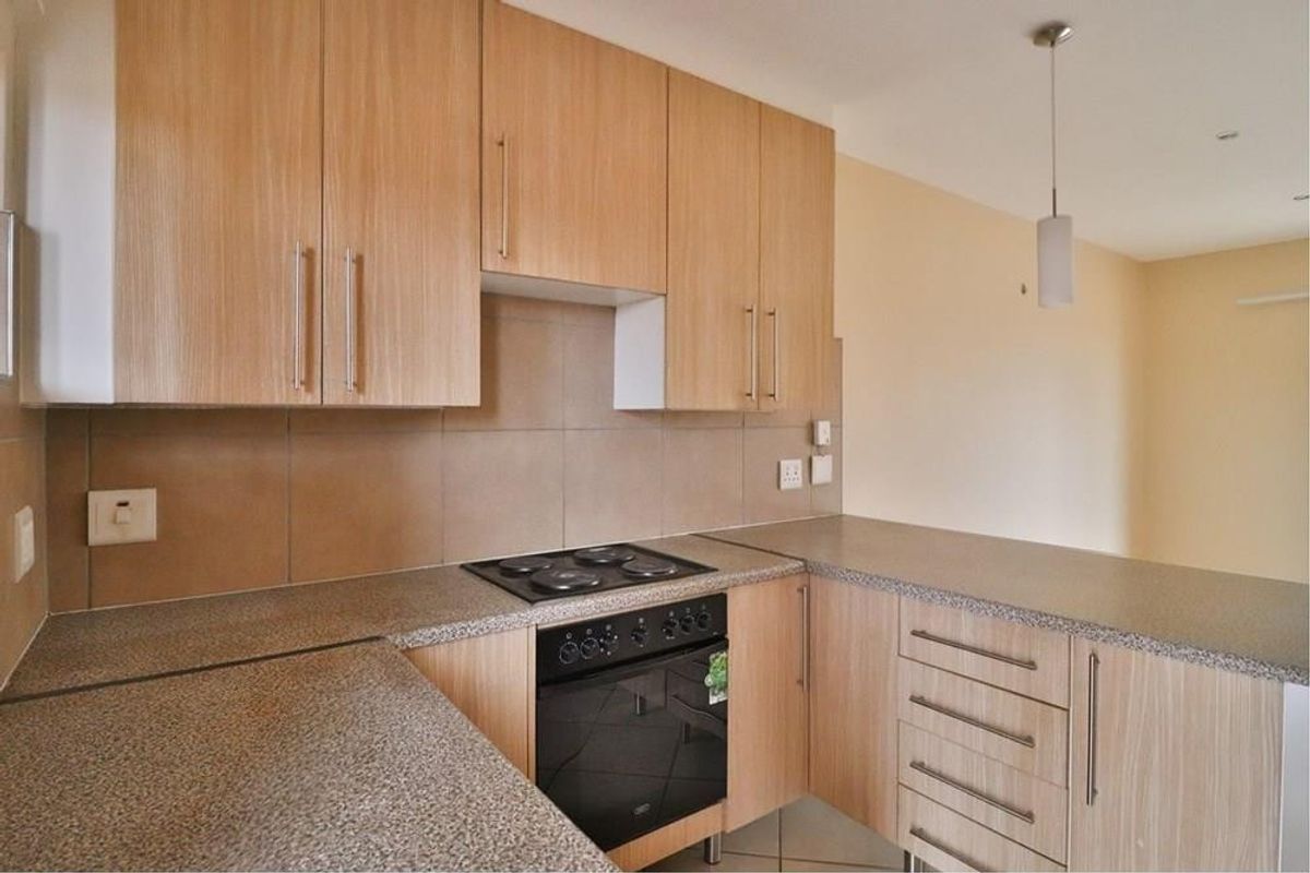 A functional kitchen featuring light wood-finish cabinetry, stone-look countertops, a built-in electric oven and hob, and a neutral tiled backsplash.