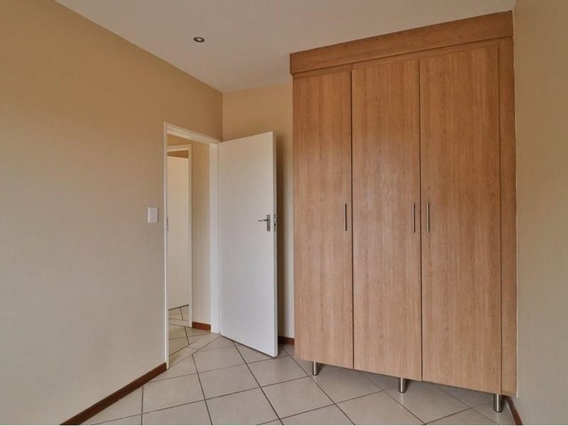 A clean, empty bedroom featuring light-toned tiled flooring and a large, modern built-in wooden wardrobe.