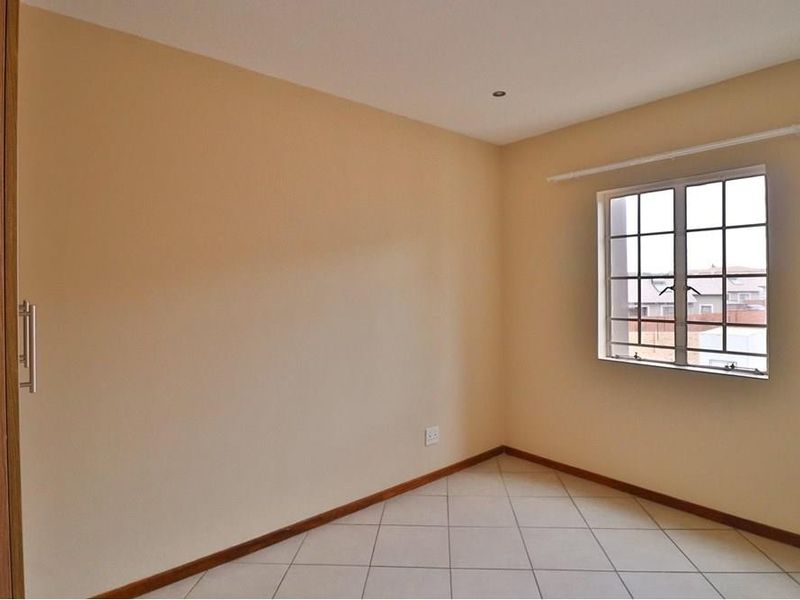 An empty bedroom featuring neutral wall paint, tiled flooring, a built-in wardrobe, and a window fitted with security bars.