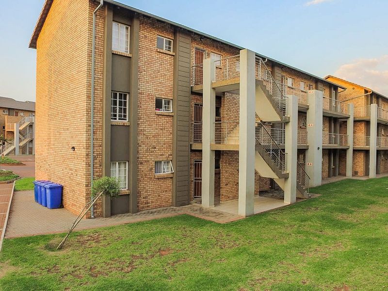 Exterior view of a multi-story apartment complex featuring face brick construction, external staircases with metal railings, and surrounding landscaped lawn areas.