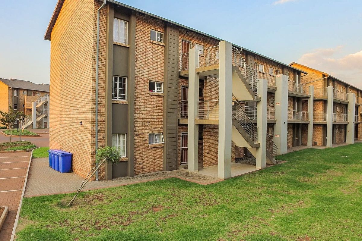 Exterior view of a multi-story apartment complex featuring face brick construction, external staircases with metal railings, and surrounding landscaped lawn areas.
