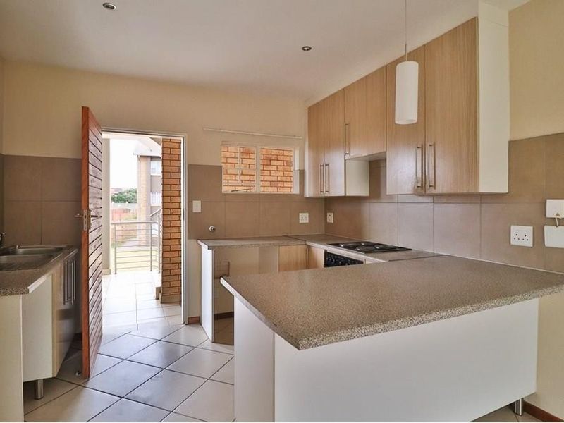 A clean, functional kitchen featuring light wood-finish cabinetry, stone-look countertops, tiled backsplash, and a breakfast bar, with direct access to an outdoor balcony.