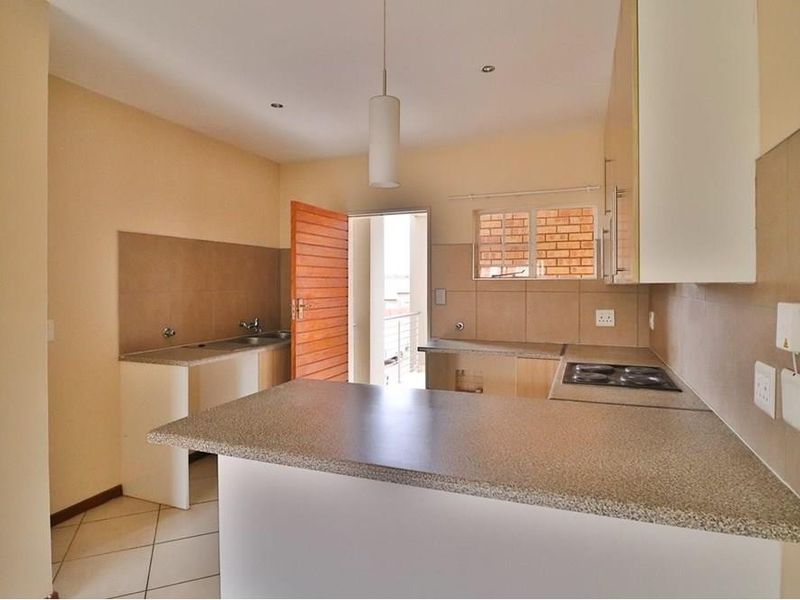 A functional, empty kitchen featuring built-in cabinetry, laminate countertops, an electric hob, and a double sink with tiled backsplash and flooring.