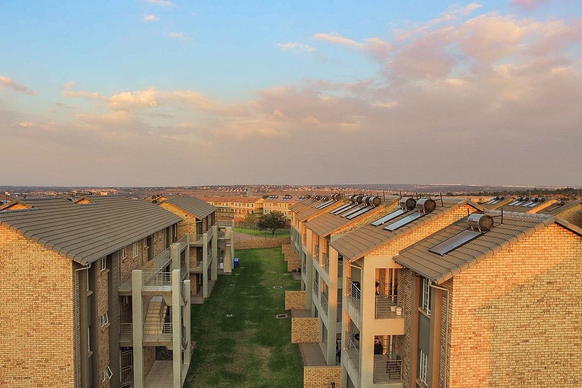 Aerial view of a residential apartment complex featuring facebrick buildings, tiled roofs with solar water heaters, and a central communal lawn area.